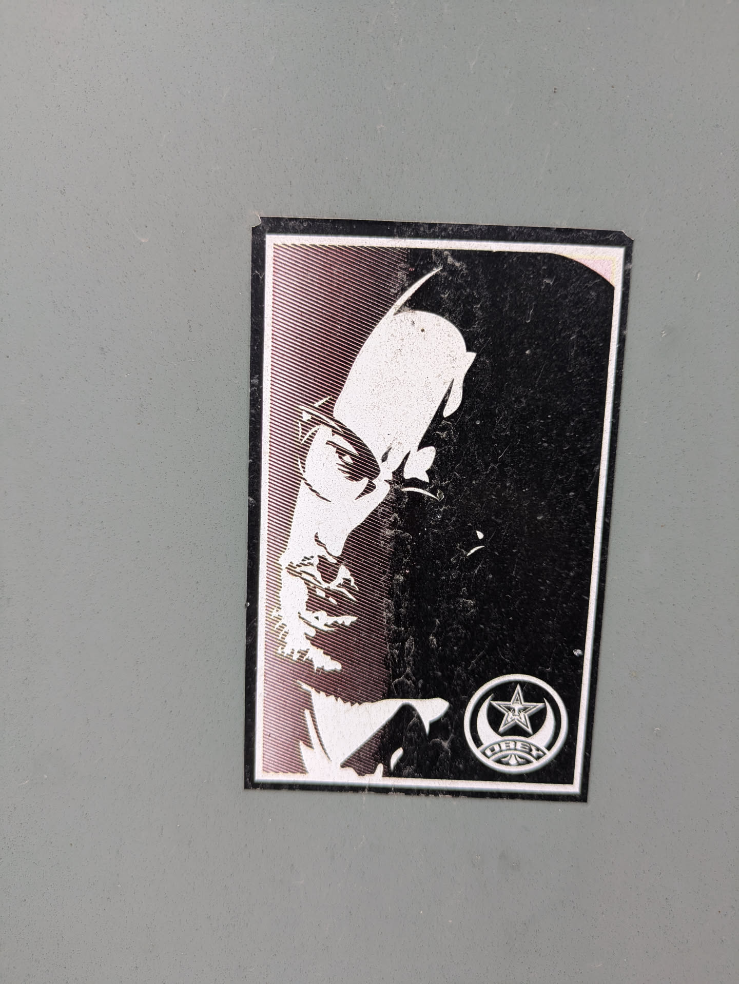 This sticker displays a black and white portrait of Malcolm X, with a section of the face rendered in a halftone pattern. A symbol with a star and crescent moon is located in the bottom right corner, possibly representing an organization or movement associated with Malcolm X.