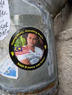 The sticker shows a man in a white Jack Daniel's t-shirt with the Malaysian flag. The text "sipping slowly, cherishing deeply" arches above him, and the text "Sukjit @ sunny was here!!!" appears below the image.