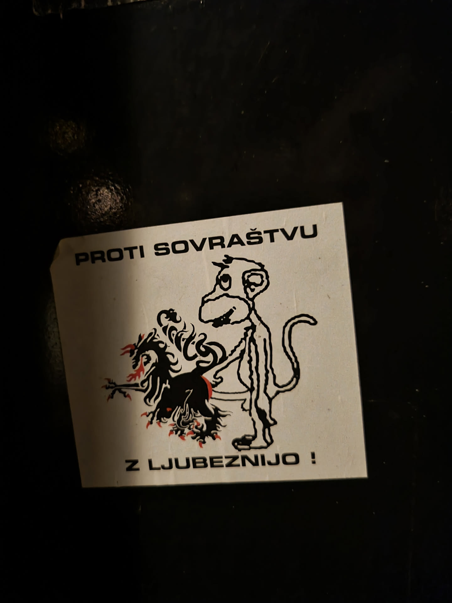 A sticker with a drawing of a monkey standing next to a burning creature. The text on the sticker says "Against hatred with love!"