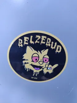 Round sticker featuring a cartoon cat with red eyes, holding a cigarette, with dripping paint effect. The text "Belzebud" is written in a dripping style above the cat. The text "EST. 2018" is written at the bottom.
