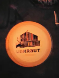Round orange sticker with an illustration of a house and the word Unkraut written below it.