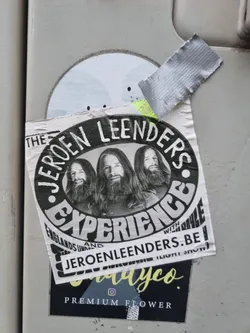 Street sticker A sticker featuring three people with long hair in black and white. The text on the sticker says 'The Jeroen Leenders Experience' and includes a website address jeroenleenders.be. There is also a logo for a company called 'dayco' at the bottom.
