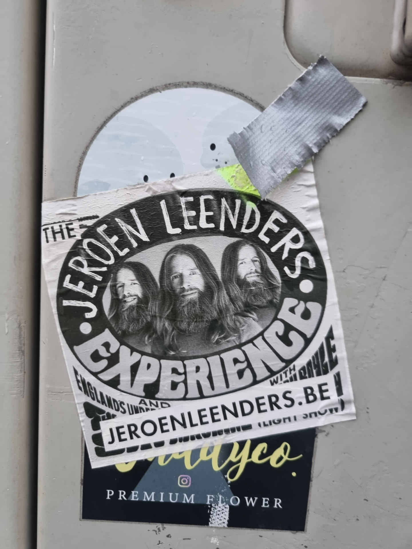 A sticker featuring three people with long hair in black and white. The text on the sticker says 'The Jeroen Leenders Experience' and includes a website address jeroenleenders.be. There is also a logo for a company called 'dayco' at the bottom.
