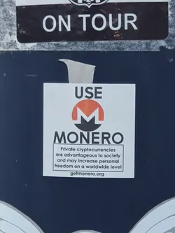 A sticker promoting Monero, a privacy-focused cryptocurrency.  The sticker features the Monero logo and text that highlights the advantages of private cryptocurrencies for society and personal freedom.  A website URL is included.