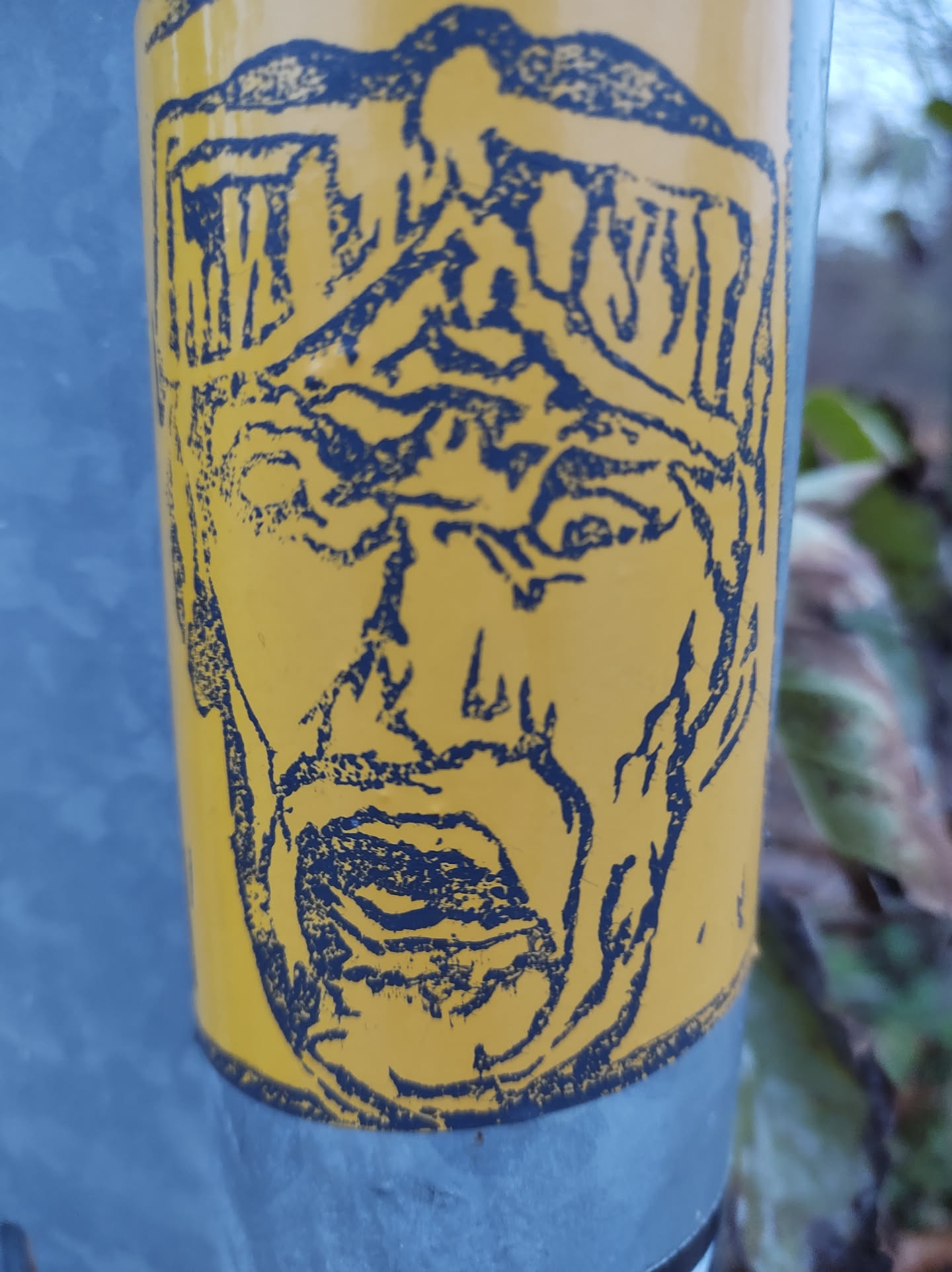 This sticker showcases an expressive face with intense features. The style is reminiscent of woodcut prints or linocuts, with strong lines and shading creating a textured effect. The color combination of yellow and blue is eye-catching, giving the sticker a vintage or retro feel. There is no visible text or QR code on the sticker itself.