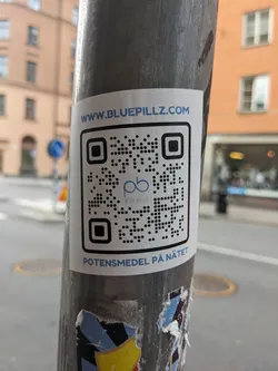 A sticker advertising a website for potency medication. The sticker has a QR code that links to www.bluepillz.com. The text on the sticker says "www.bluepillz.com" and "Potensmedel på nätet", which translates to "Potency medication online".