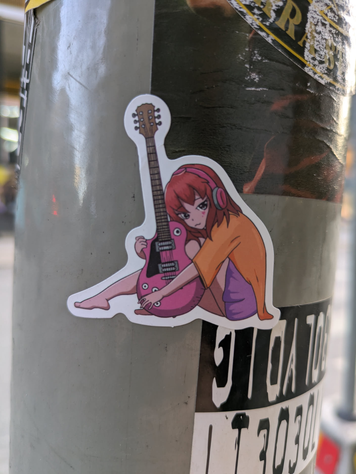 A sticker featuring an anime-style illustration of a girl with headphones sitting with a pink electric guitar. 