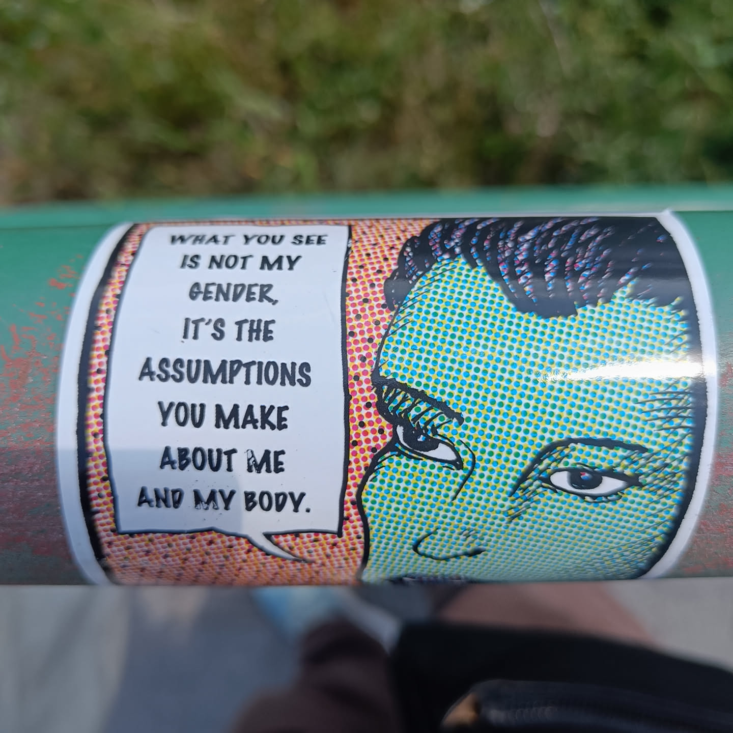 A sticker with a pop art style illustration of a person's face and a speech bubble with text. The text challenges gender assumptions.