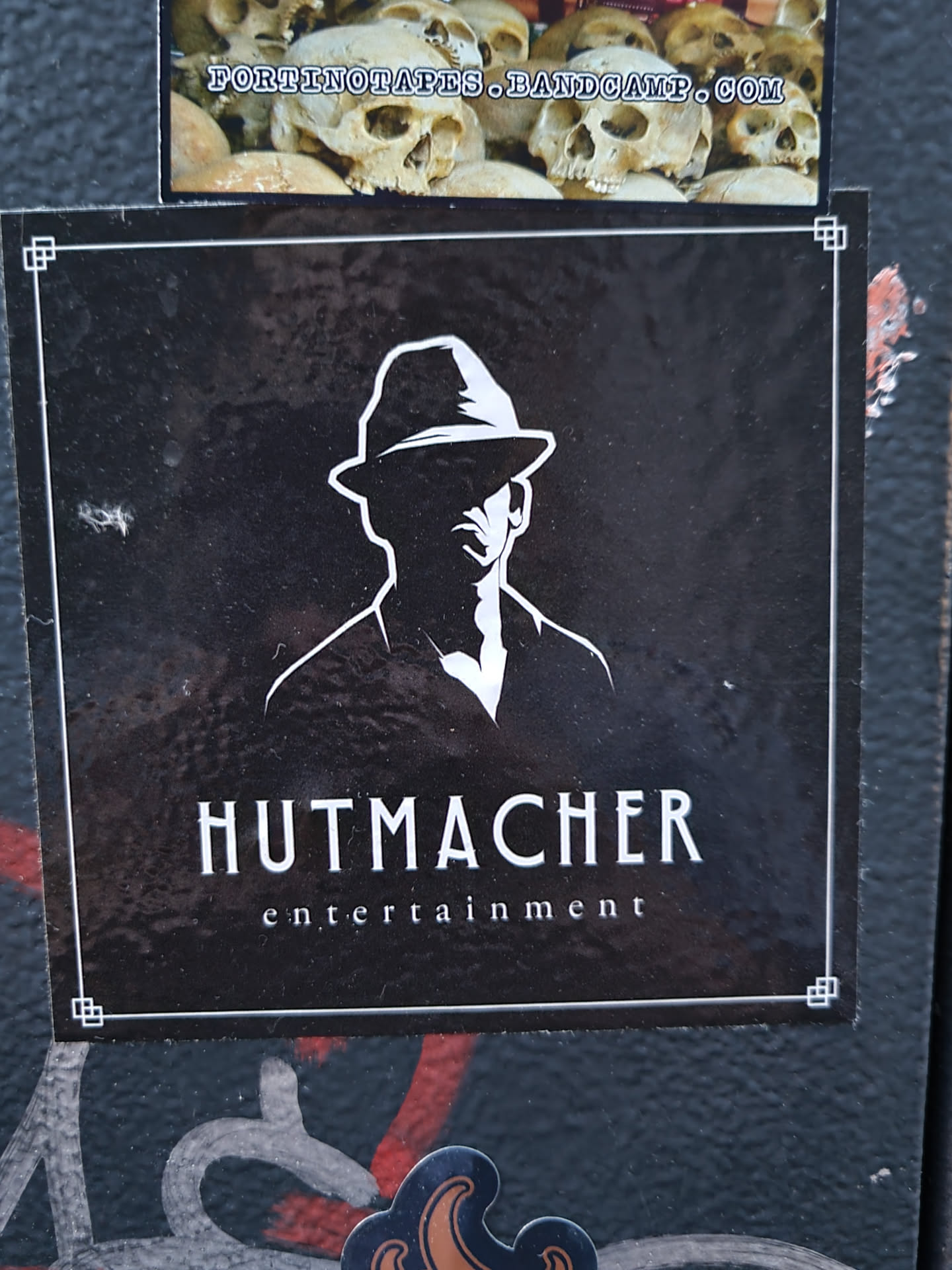 Black and white sticker featuring a silhouette of a man in a fedora hat. The text 'Hutmacher entertainment' is written below the image.