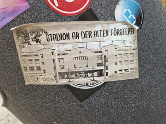 A sticker depicting the Stadium an der Alten Försterei, home of 1. FC Union Berlin. The sticker is in black and white and shows a picture of the stadium with the name written at the top.  There is also a logo of the team at the bottom.