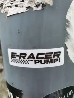 A black and white sticker with the text "E-RACER by PUMP!" and a checkered flag pattern. The sticker is affixed to a gray pole.