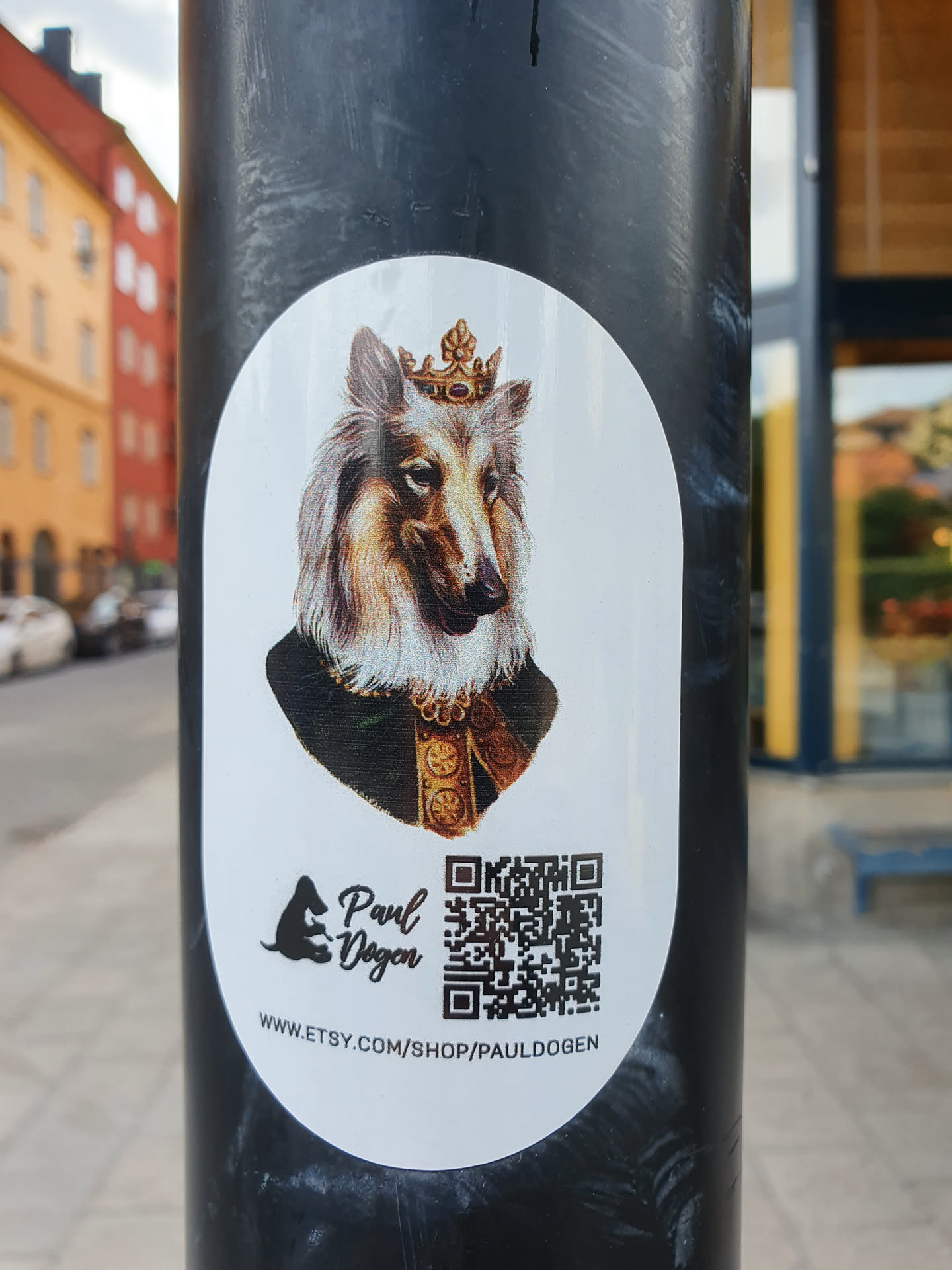 Oval sticker featuring a majestic Collie dog wearing a crown, depicted in a regal portrait style.  The sticker includes the artist's logo, name (Paul Dogen), and a QR code linking to their Etsy shop.