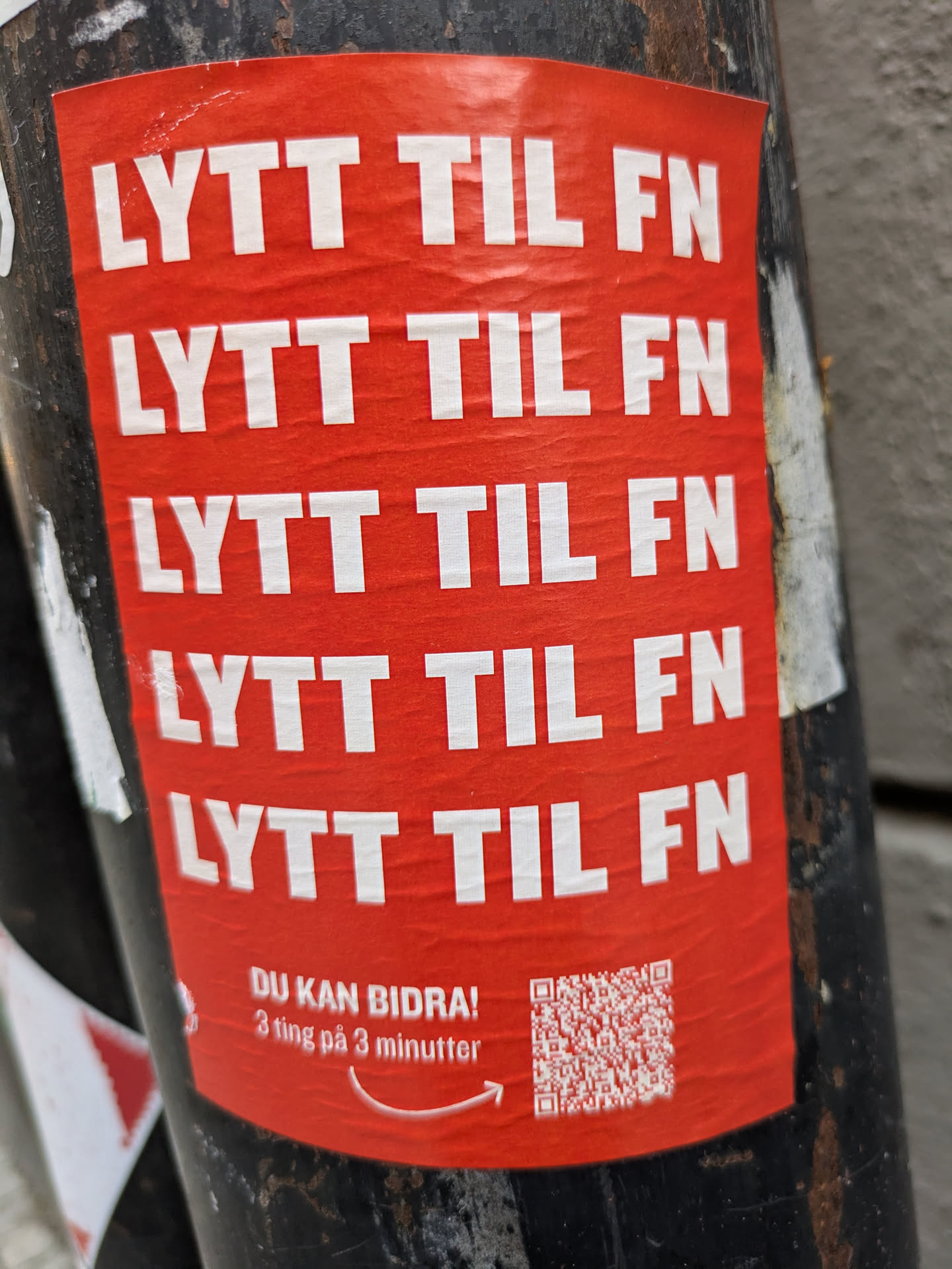 A red sticker with the text "LYTT TIL FN" (Listen to the UN) repeated five times.  At the bottom, it says "DU KAN BIDRA! 3 ting på 3 minutter" (You can contribute! 3 things in 3 minutes) and contains a QR code.