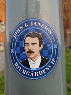 A round sticker featuring an illustration of John G Jansson, with Djurgårdens IF written around it. The background is a blue and white checkered pattern.