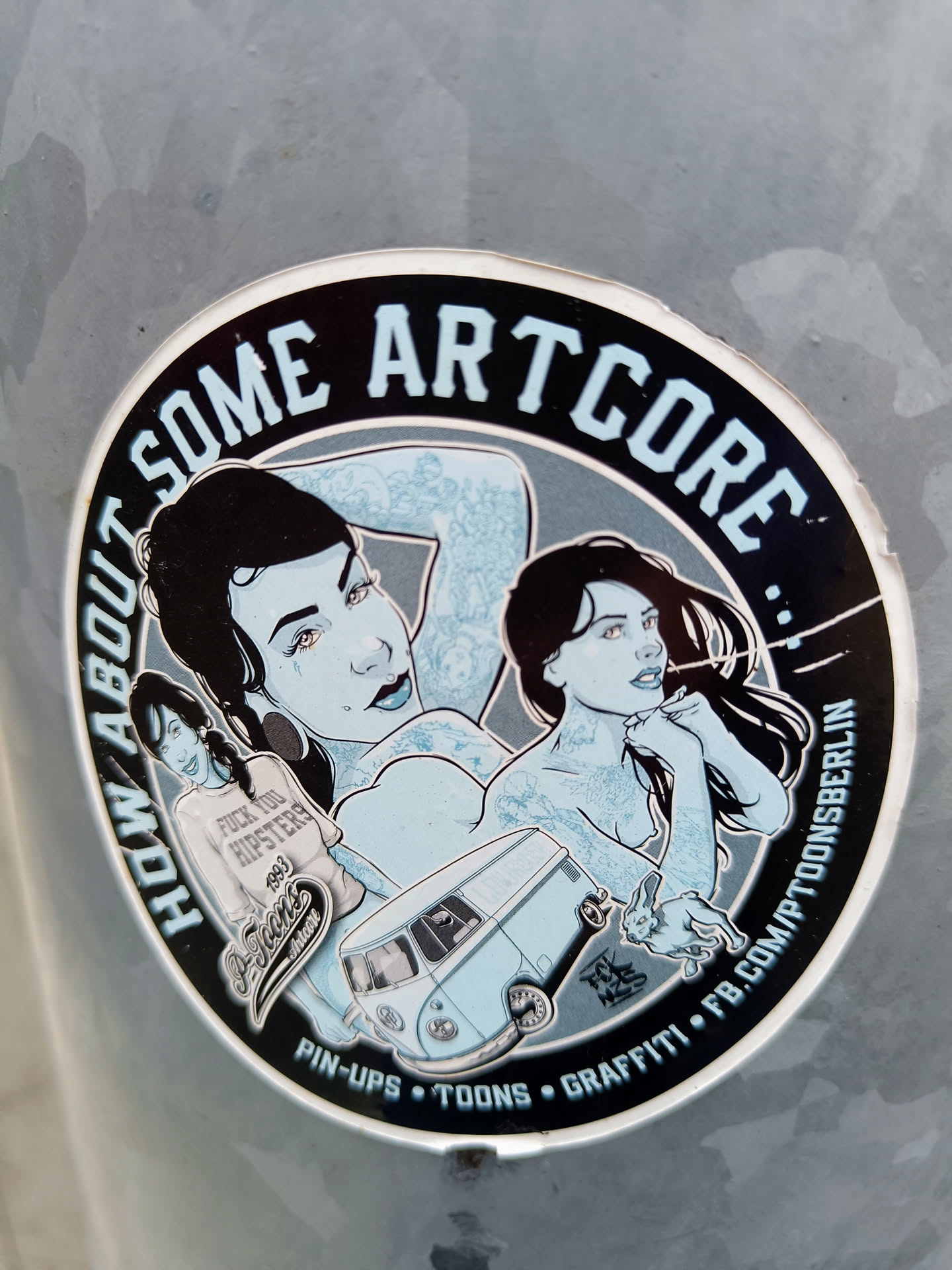 Round sticker featuring pin-up style illustrations, a VW bus, and a rabbit.  The text "How About Some Artcore" is prominently displayed, along with additional text indicating a focus on pin-ups, toons, and graffiti.  A Facebook link is also present.