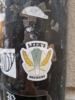 A sticker featuring the Leek's Brewery logo. The logo depicts a leek with wheat stalks on either side, set against a mountain backdrop. The text 'LEEK'S' is at the top, and 'BREWERY' is at the bottom. 