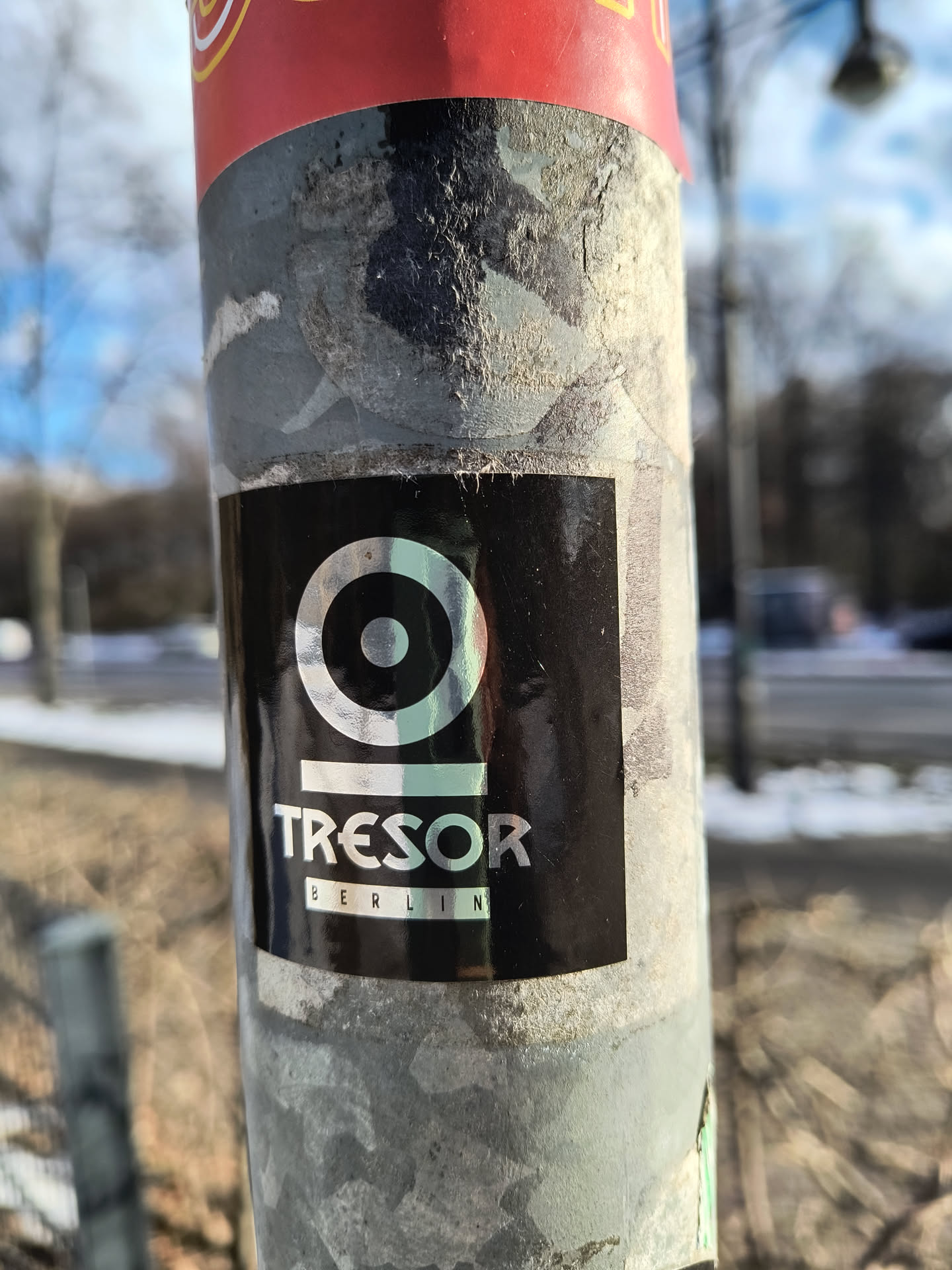 A black sticker is affixed to a pole, displaying the logo of Tresor Berlin. The logo features a concentric circle design above the word 'TRESOR' and 'BERLIN' printed below in smaller font size.