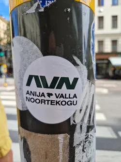 A white round sticker with a dark green logo and text. The logo is a stylized "AVN". The text says "ANIJA \\\\ VALLA NOORTEKOGU".