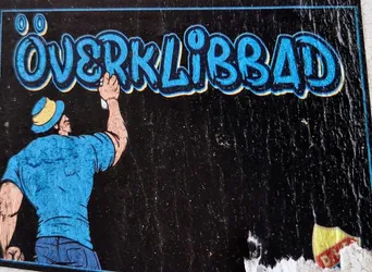 A sticker featuring a muscular man painting graffiti that says "ÖVERKLIBBAD" on a black background. The style is reminiscent of comic book art.