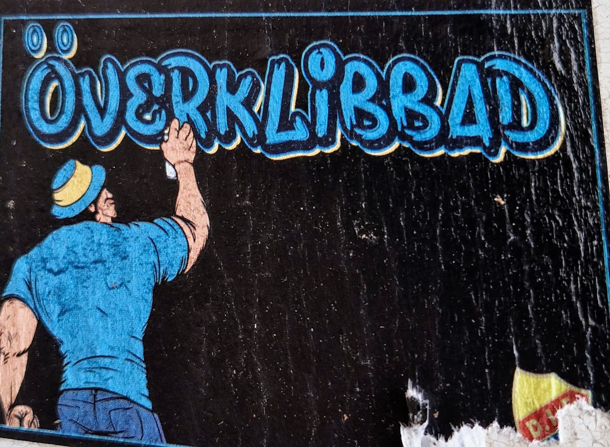 A sticker featuring a muscular man painting graffiti that says "ÖVERKLIBBAD" on a black background. The style is reminiscent of comic book art.