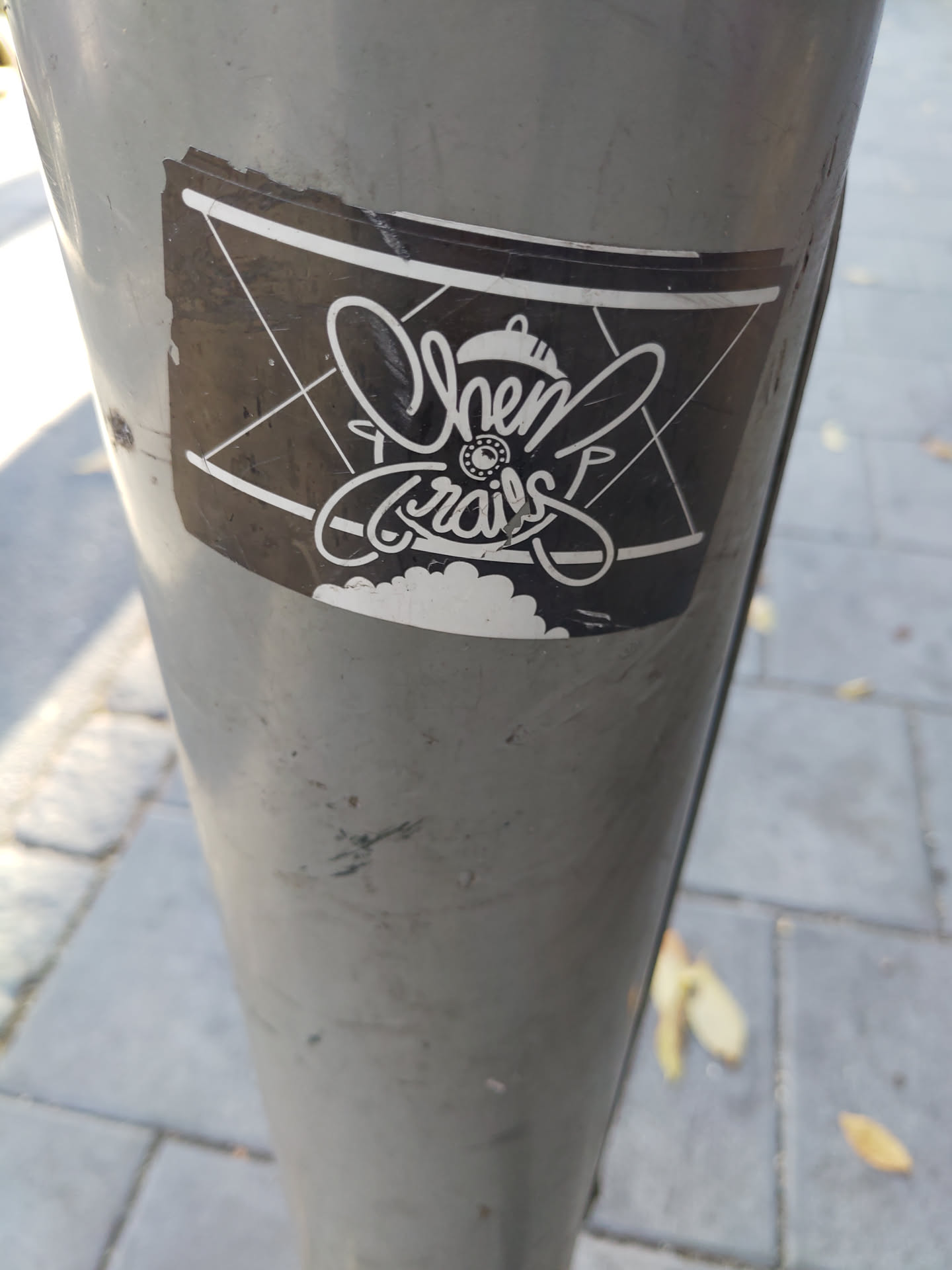 Black and white sticker with the words Chem Trails in a stylized font. The design includes an airplane-like shape and some other graphic elements. The sticker is slightly damaged.