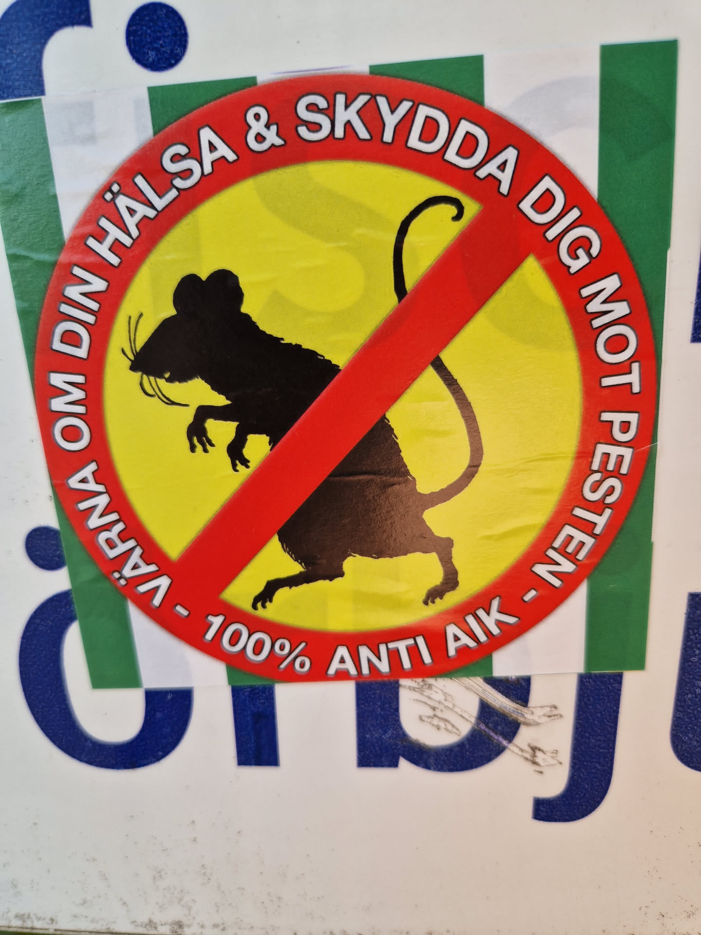A round sticker with a red circle and a cross over a black silhouette of a rat on a yellow background. The text around the circle says "VÄRNA OM DIN HÄLSA & SKYDDDA DIG MOT PESTEN - 100% ANTI AIK" which translates to "Protect your health & protect yourself against the plague - 100% ANTI AIK".