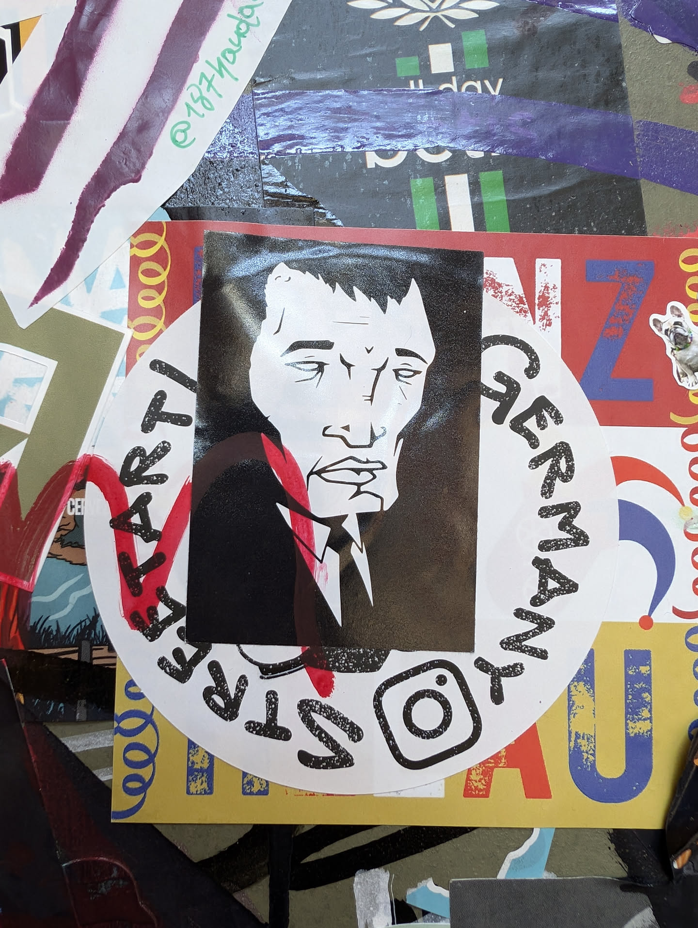 This sticker features a black and white illustration of a man with a serious expression. He appears to be wearing a suit. The style is reminiscent of political cartoons or caricatures. The circular sticker has the word 'GERMAN' written around the illustration, suggesting a possible connection to Germany or German culture. An Instagram logo is printed on the sticker suggesting an artist's social media handle.