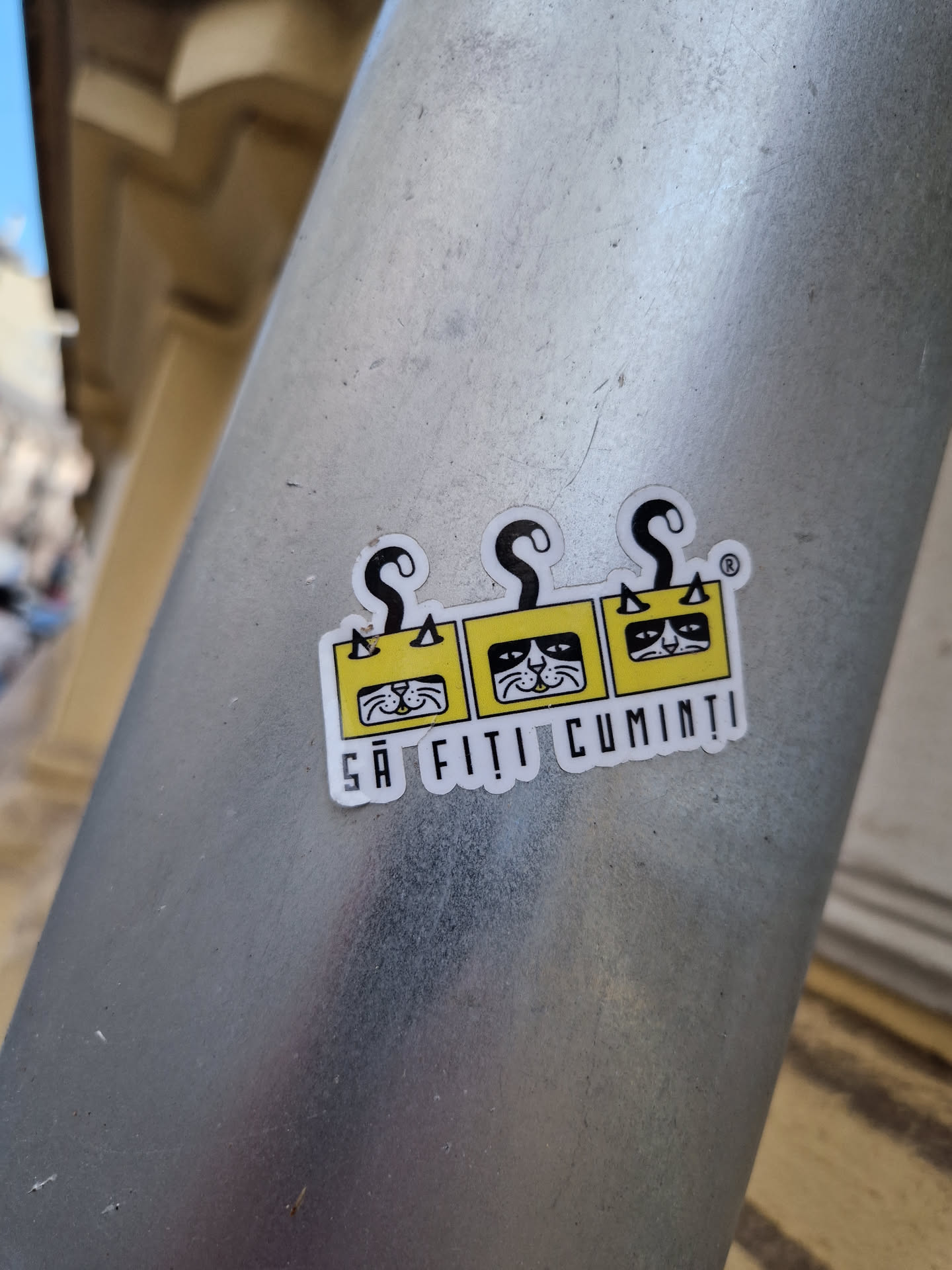 A yellow sticker with three stylized cats and Romanian text: "Să fiți cuminți" which translates to "Behave yourselves".