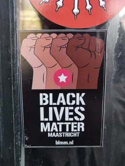A Black Lives Matter sticker featuring four fists of different skin tones raised in solidarity.  The sticker has a pink star and the website blmm.nl.