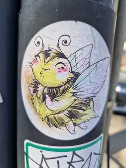 A cute, cartoonish bee with large eyes and wings. It's drawn in a whimsical style with yellow and brown fur and pastel-colored wings. The bee appears happy and friendly.