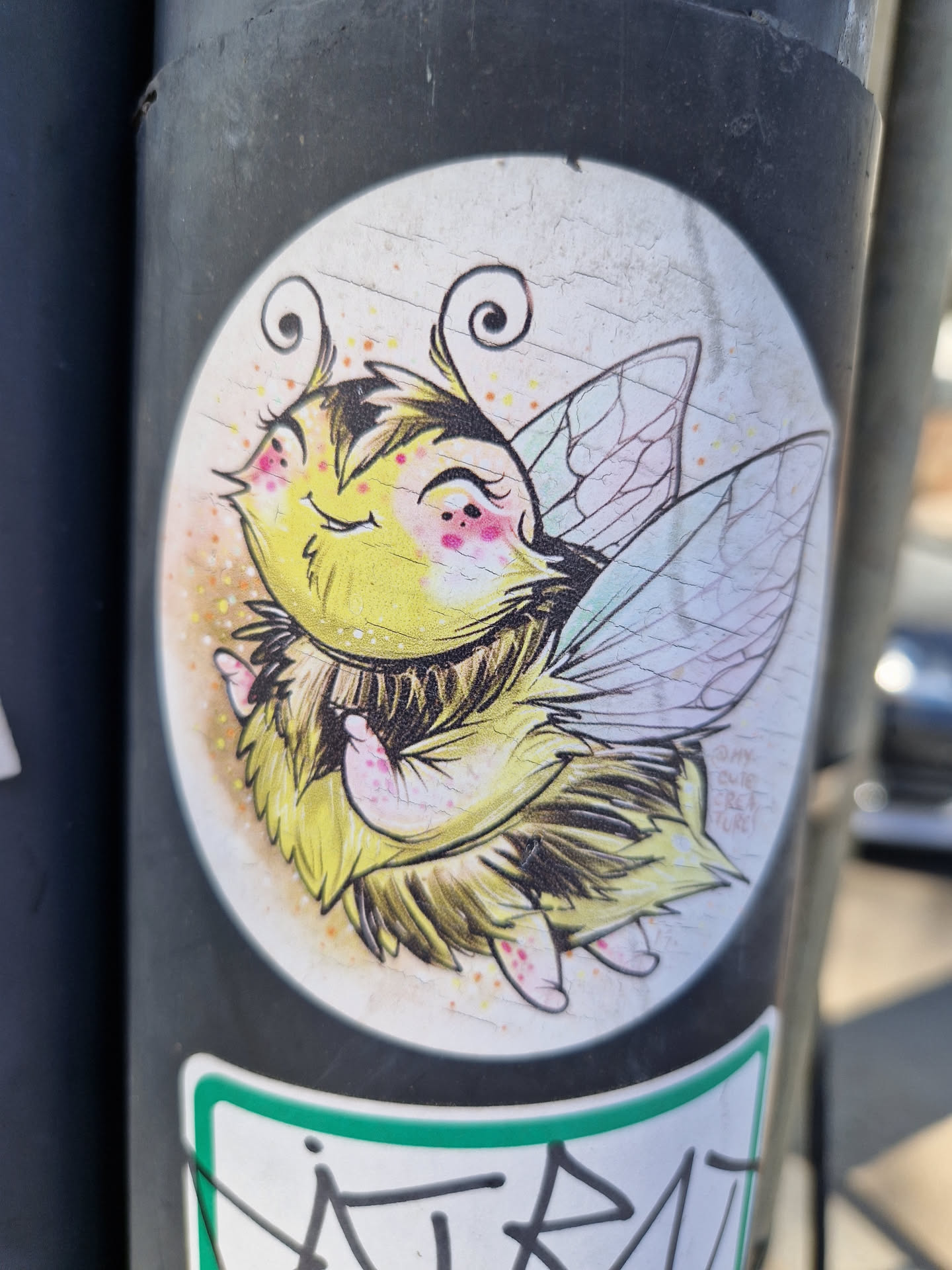 A cute, cartoonish bee with large eyes and wings. It's drawn in a whimsical style with yellow and brown fur and pastel-colored wings. The bee appears happy and friendly.