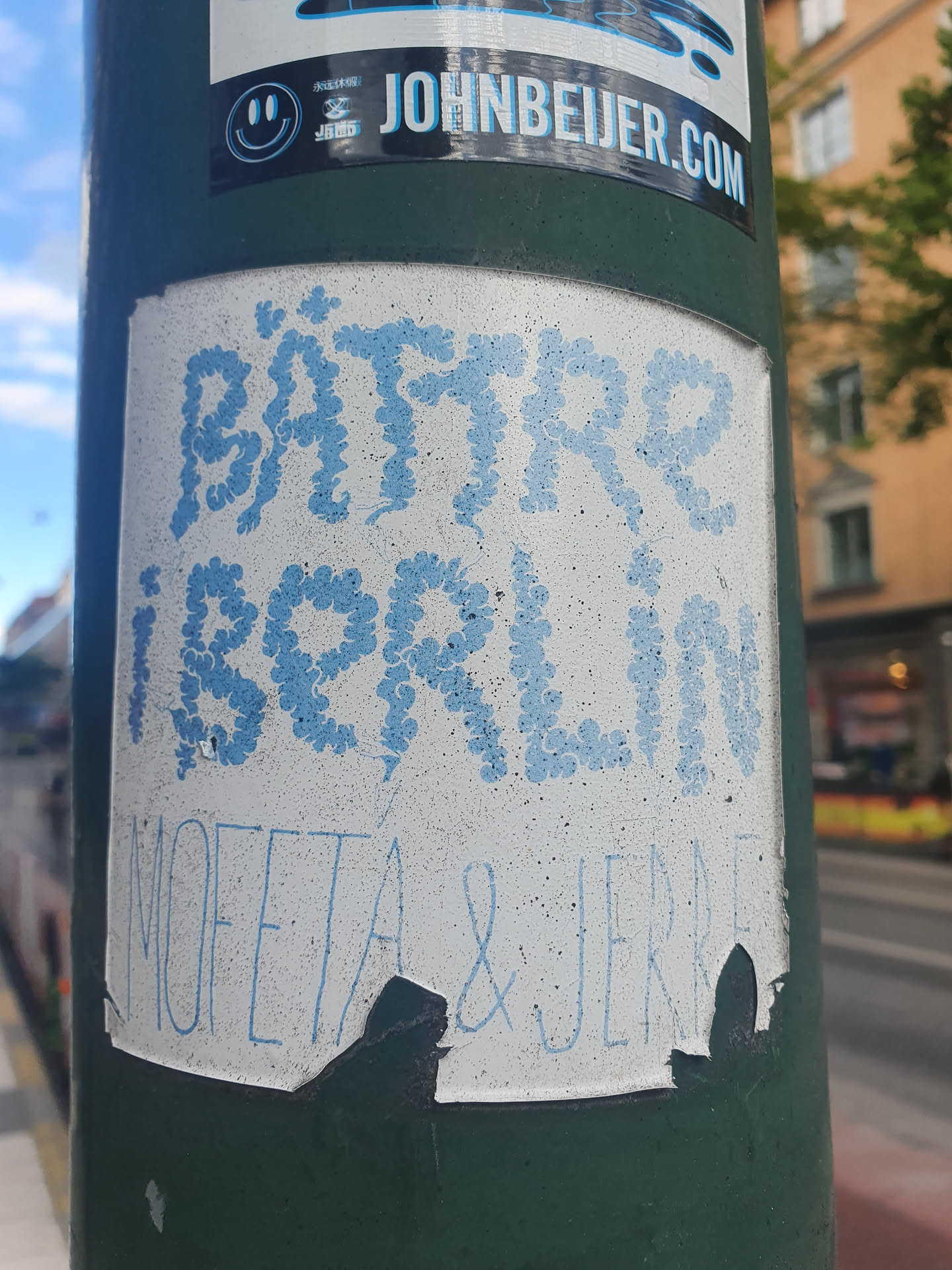 A sticker with the text "BÄTTRE I BORLÄN" written in light blue stylized lettering. Below it, it says "MOFETA & JENNE". The sticker is slightly damaged around the edges.