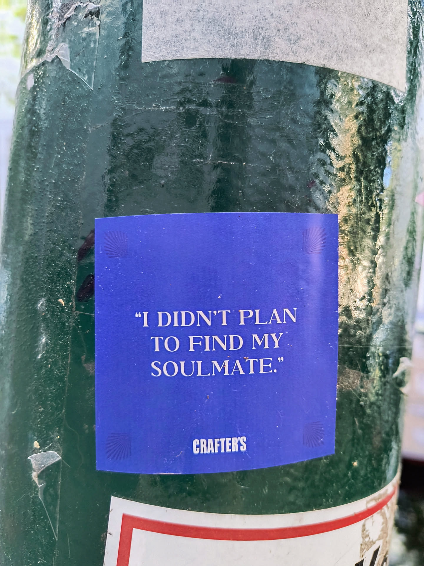 A blue sticker on a green pole reads, "I DIDN'T PLAN TO FIND MY SOULMATE." and "Crafter's" is written on the bottom right corner of the sticker.