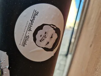 Round sticker featuring a black and white illustration of a person's face and text. The text mentions "Thangach - Werke" and "Hofbau-Rotzbuam".