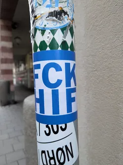 Street sticker A rectangular sticker wrapped around a metal pole. The sticker features horizontal blue bands across the top and bottom, framing a white center. Bold blue sans-serif block lettering in the center displays 'FCK' on the upper line and 'HIF' on the lower line, commonly associated with football rivalry slogans against HIFK.