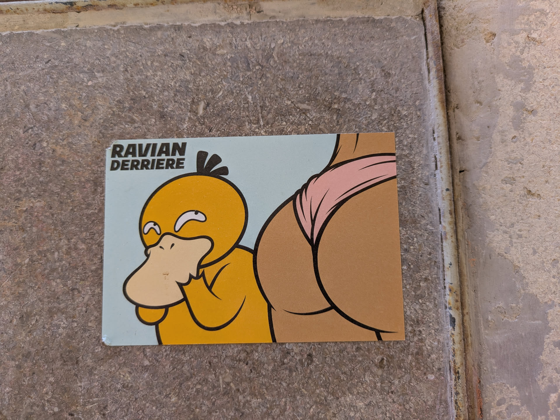 The sticker shows a bewildered Psyduck next to an illustration of a backside wearing a pink bikini bottom. The text 'RAVIAN DERRIERE' is at the top left.