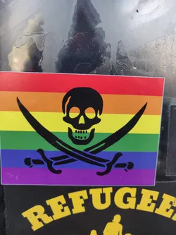 A sticker featuring a rainbow-colored pirate flag with a black skull and crossbones in the center. Below the flag, the word "REFUGEE" is written in yellow uppercase letters.