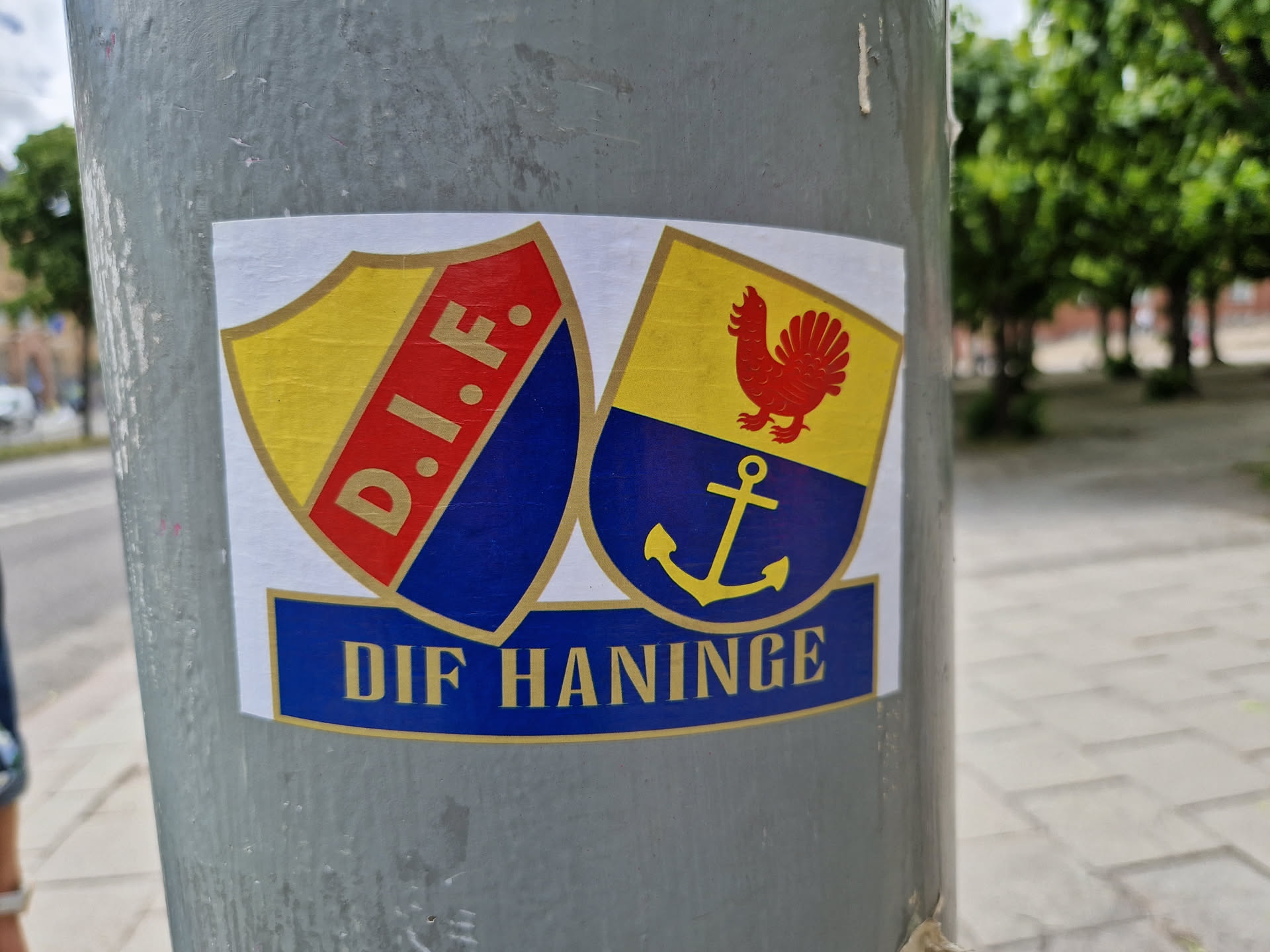 A sticker featuring two shields, one with the letters D.I.F. and the other with a rooster and an anchor.  The text "DIF HANINGE" is at the bottom.