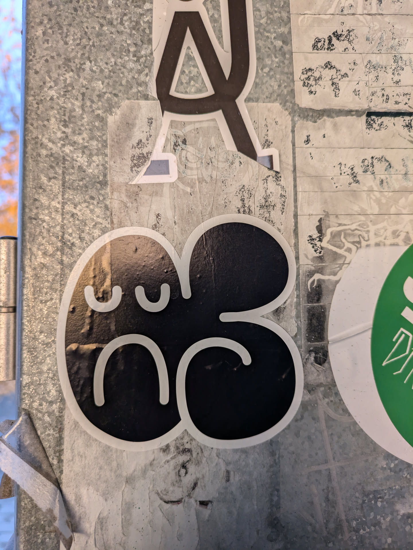 This sticker features a simple black design shaped like a deformed flower or blob with a cute, slightly sad face.  The style is minimalist and cartoonish.