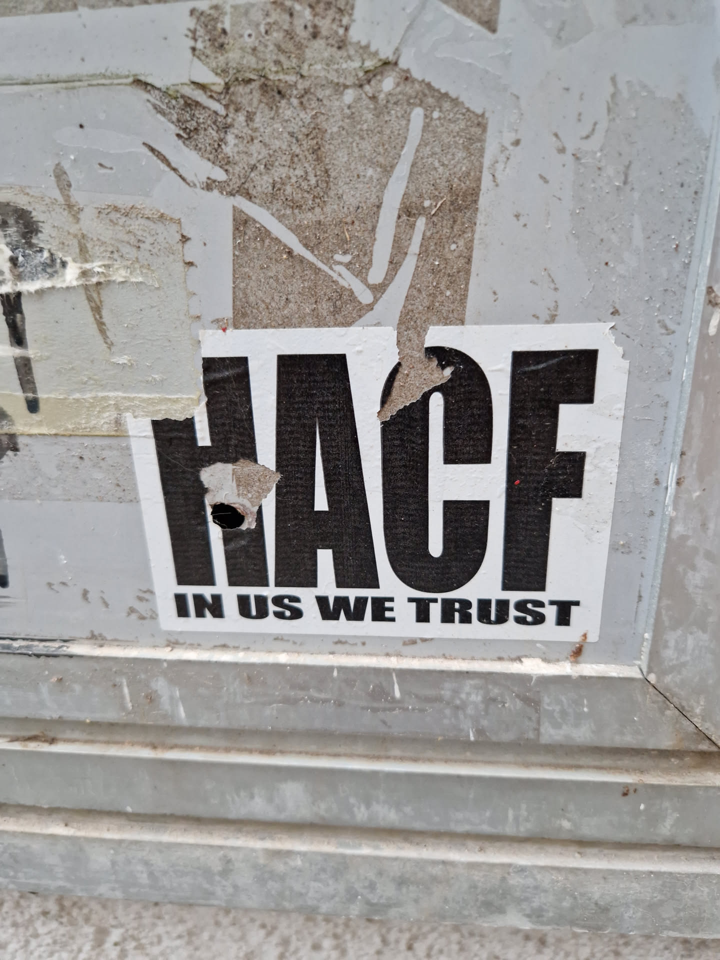 A sticker with the acronym HACF and the text "In us we trust". The sticker is slightly damaged.