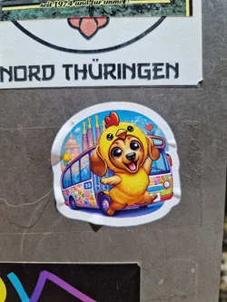A sticker featuring an illustration of a dog wearing a chicken costume, standing on a colorful psychedelic bus.  The background includes what looks like a stylized cityscape or landmark.