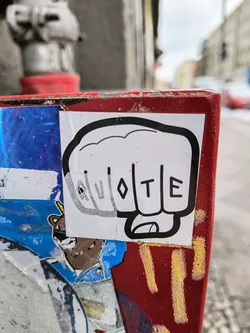 A sticker depicting a fist with the word VOTE written on the knuckles. The sticker is placed on a red surface covered in other stickers.