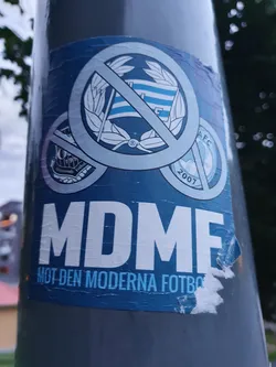 A sticker expressing opposition to modern football. It features a crossed-out logo, possibly representing a football club, and the acronym MDMF, which translates to "Against Modern Football" in Swedish.
