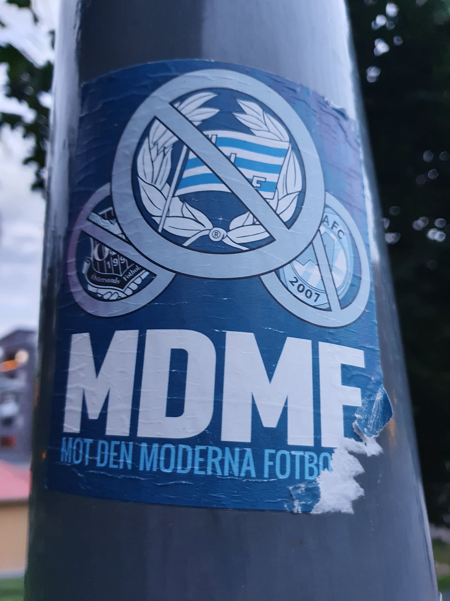 A sticker expressing opposition to modern football. It features a crossed-out logo, possibly representing a football club, and the acronym MDMF, which translates to "Against Modern Football" in Swedish.