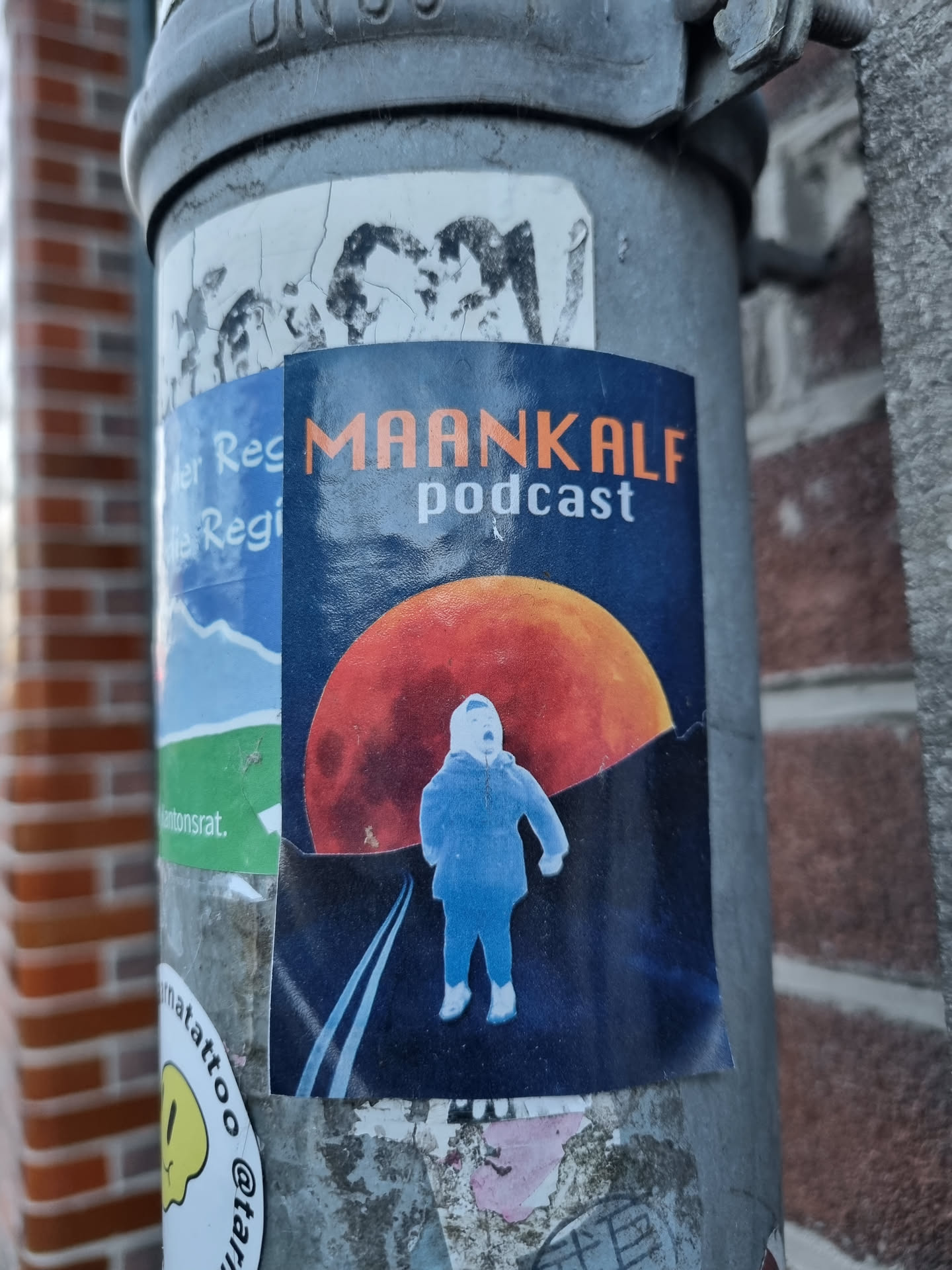 A sticker featuring a stylized illustration of a person standing on a road with a large moon in the background. The text "MAANKALF podcast" is prominently displayed.