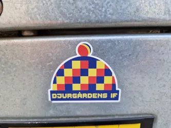 A sticker featuring a stylized beanie with a checkered pattern in red, yellow, and blue. The text "DJURGÄRDENS IF" is visible at the bottom of the sticker.