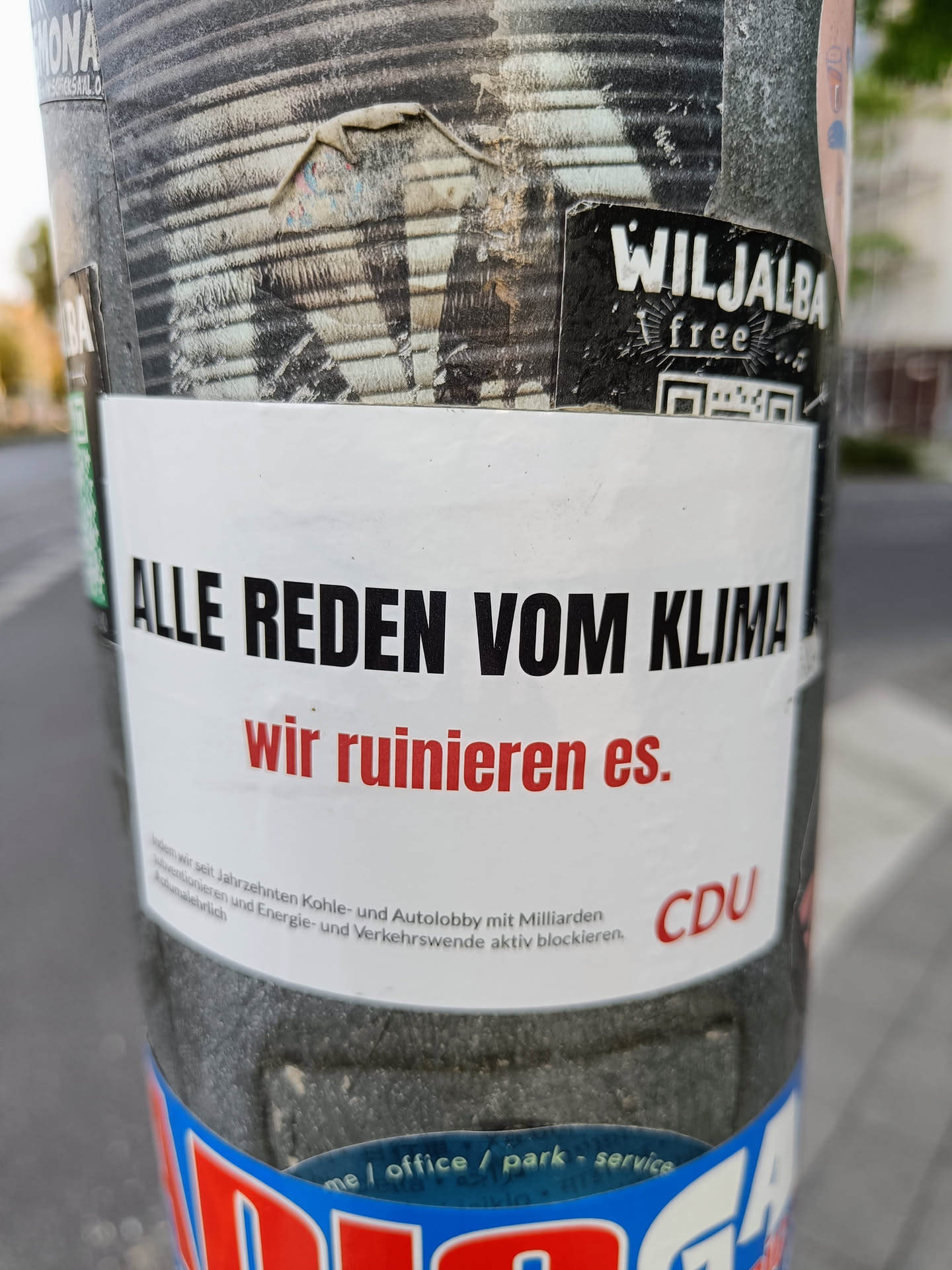 A sticker on a pole with the text "Alle reden vom Klima, wir ruinieren es." (Everyone talks about the climate, we are ruining it.)  The sticker also contains the CDU logo. 