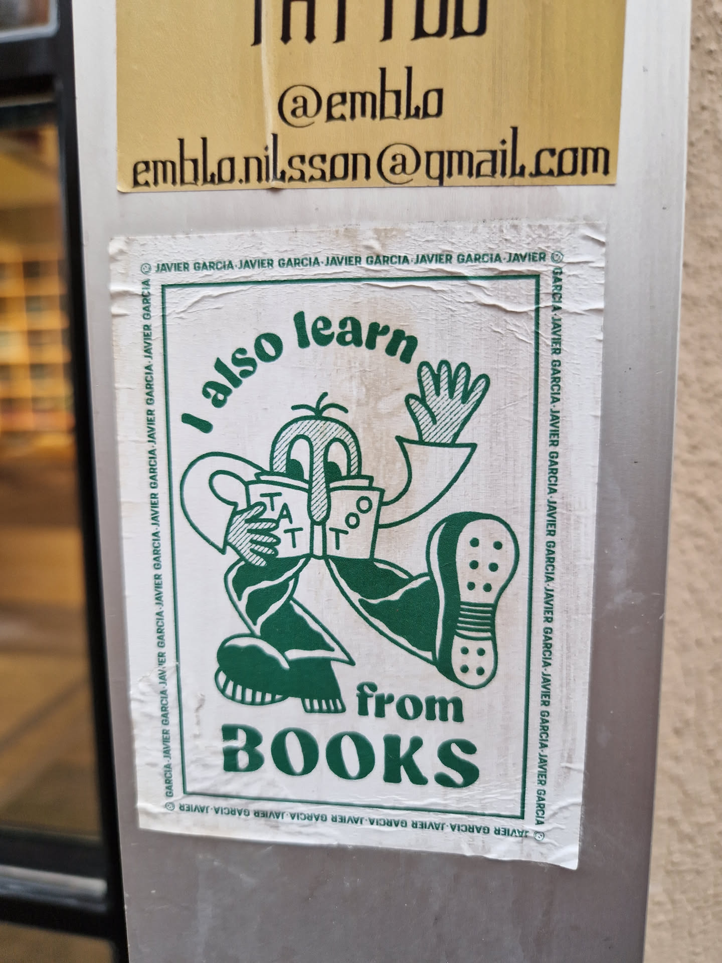 A sticker featuring a cartoon character reading a book with the text "I also learn from BOOKS". The sticker has a green and white color scheme and a minimalist design.  The artist's email is visible on a sticker above this one.