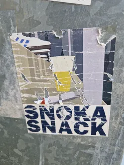 A torn sticker with an illustration of a drink and the text Snoka Snack. The sticker shows signs of wear and tear, with parts of the image missing.