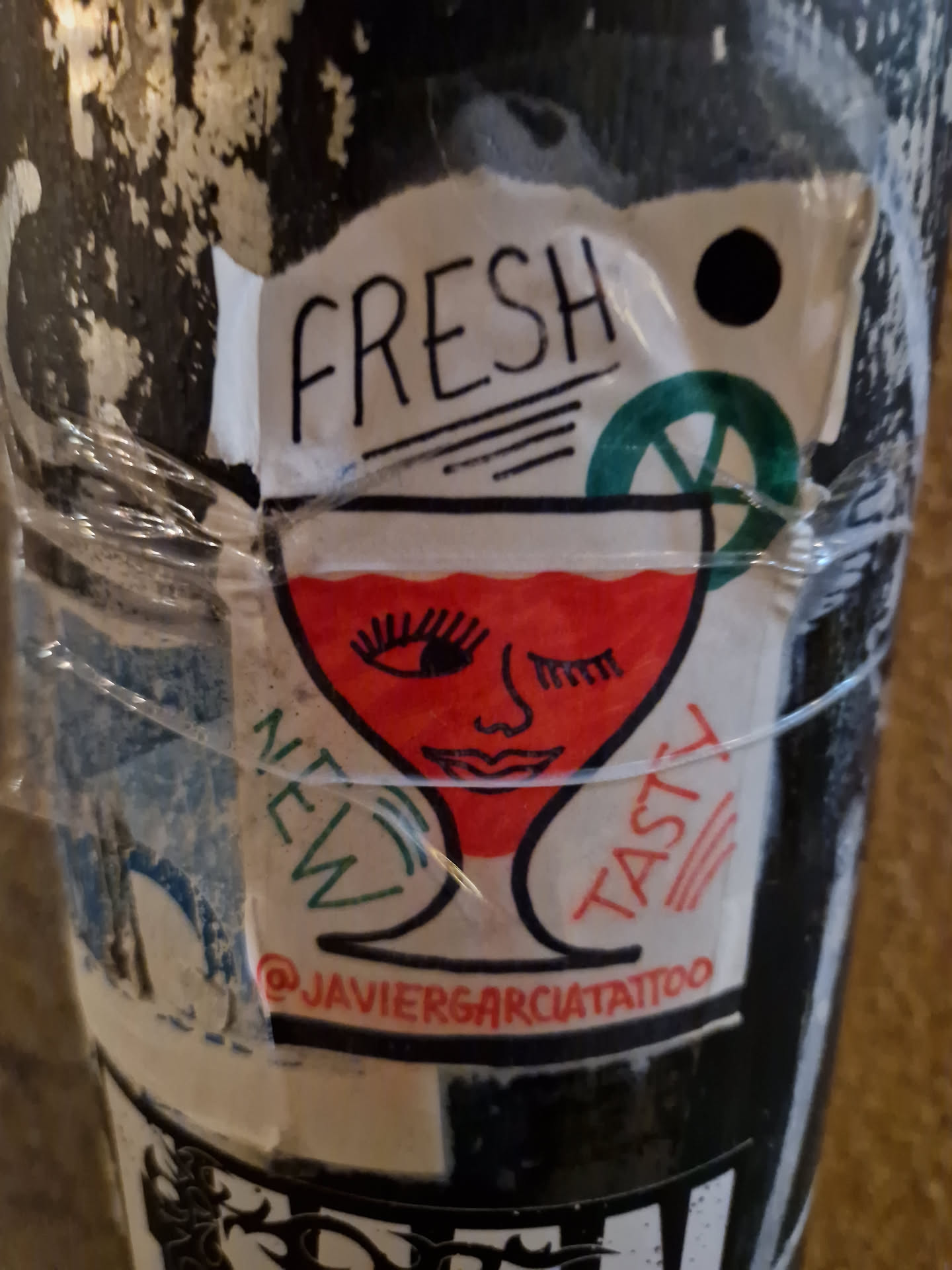 A sticker featuring an illustration of a winking glass of cocktail. The words "Fresh", "New", and "Tasty" surround the glass. The sticker also includes the text "@javiergarciatattoo", which seems to be a social media handle. 